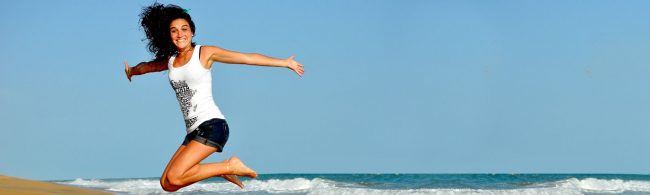 Frau springt vor Freude am Strand, inspiriert von gesunder Ernährung und Fitness.