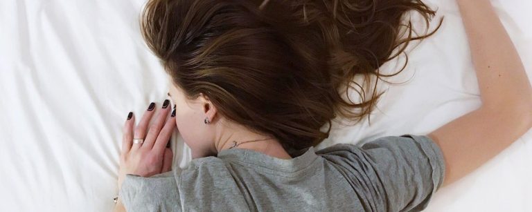 Frau schläft auf einem Bett, umgeben von weißer Bettwäsche.