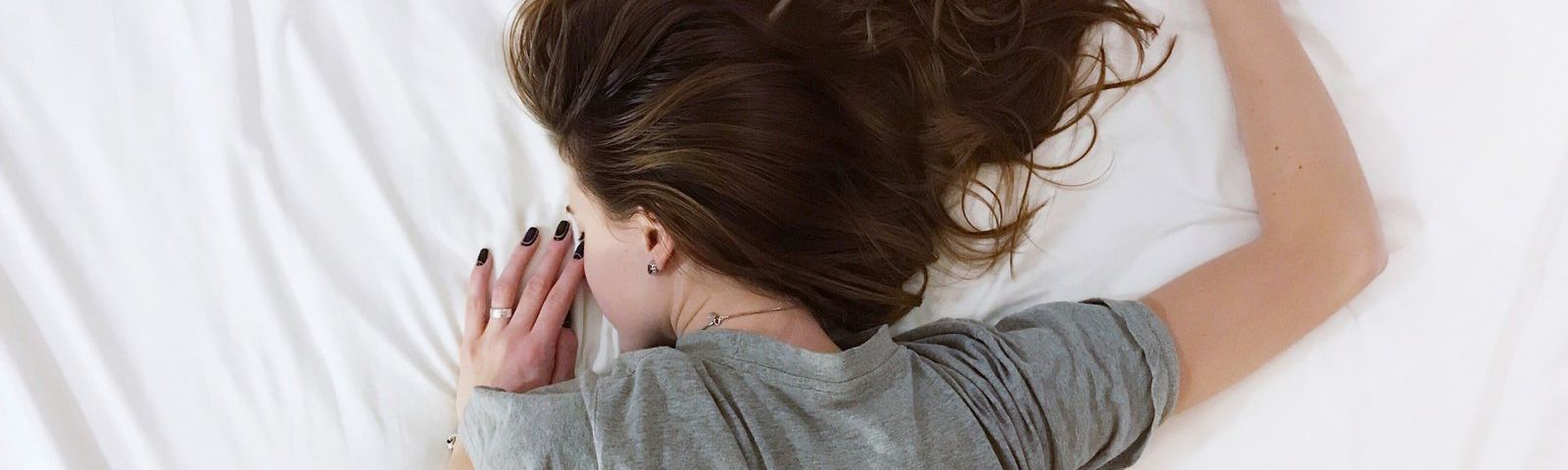 1708-tips-om-beter-te-kunnen-slapen Frau schläft auf einem Bett, umgeben von weißer Bettwäsche.