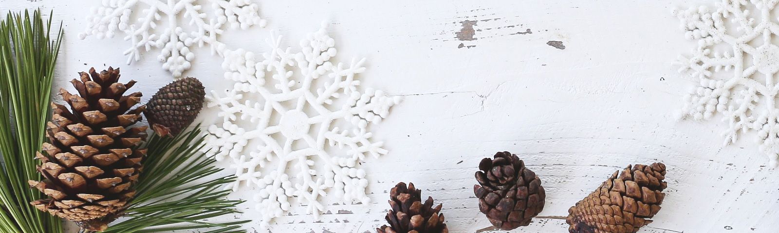 Weihnachtliche Dekoration mit Tannenzapfen und Schneeflocken auf weißem Holzhintergrund.