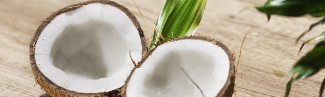 Eine Kokosnuss geöffnet auf einem Holztisch mit einem Blatt.