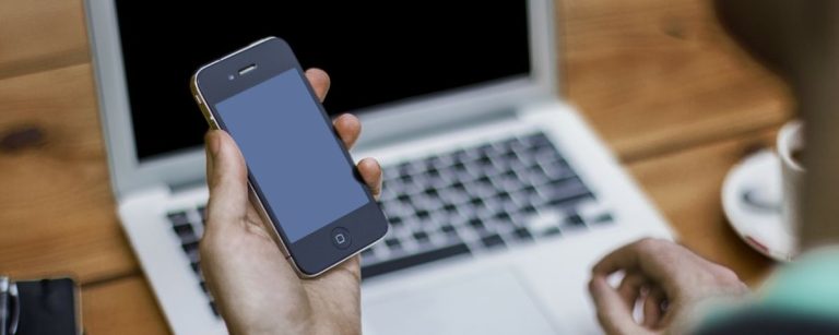 Person hält Smartphone vor Laptop. Fitness-Ernährungs-Firma.