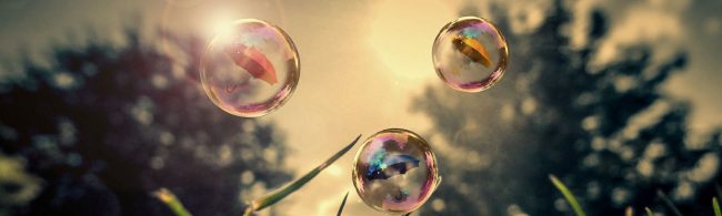 BF-ademen-1600×480 Sechs bunte Regenschirme schweben in Wasserblasen über saftigem Gras.