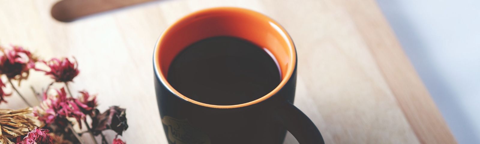 BF-cafeine-1600×480 Gesunder Kaffee neben getrockneten Blumen auf Holzunterlage.
