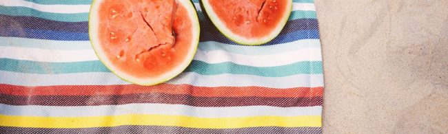 Zwei Wassermelonen auf einem gestreiften Handtuch am Strand – perfekt für eine gesunde Fitness-Ernährung.