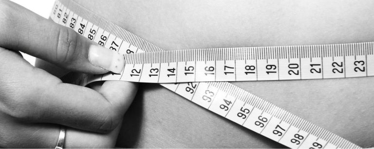 Eine Hand misst die Taille mit einem Maßband, was Gewichtsverlust und Fitnessziele symbolisiert.