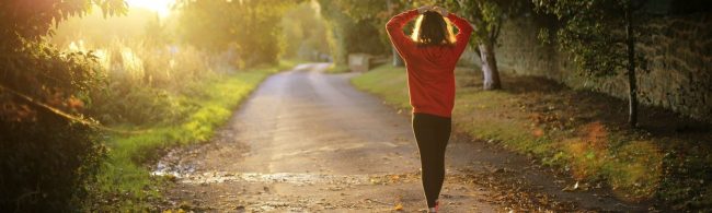 Junge Frau in rotem Hoodie joggt im goldenen Sonnenlicht auf einer Landstraße.
