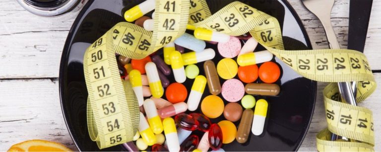 Gesunde Ernährung und Gewichtsverlust mit Medikamenten und Messband auf schwarzem Teller.