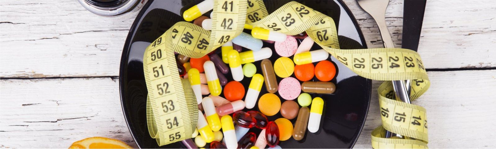 Gesunde Ernährung und Gewichtsverlust mit Medikamenten und Messband auf schwarzem Teller.