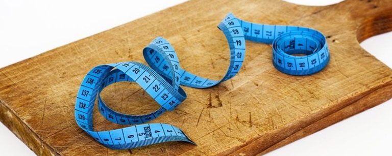 Blaues Maßband auf Holzbrett, symbolisiert Fitness und gesunde Ernährung.