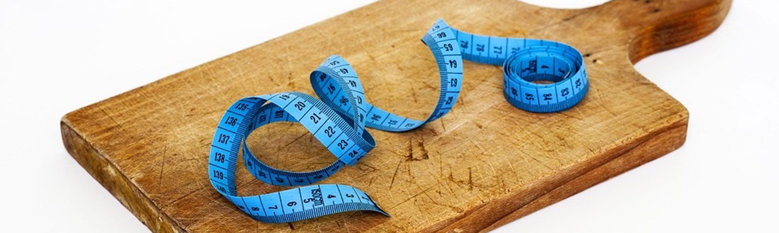 eten-in-de-avond-g_1 Blaues Maßband auf Holzbrett, symbolisiert Fitness und gesunde Ernährung.