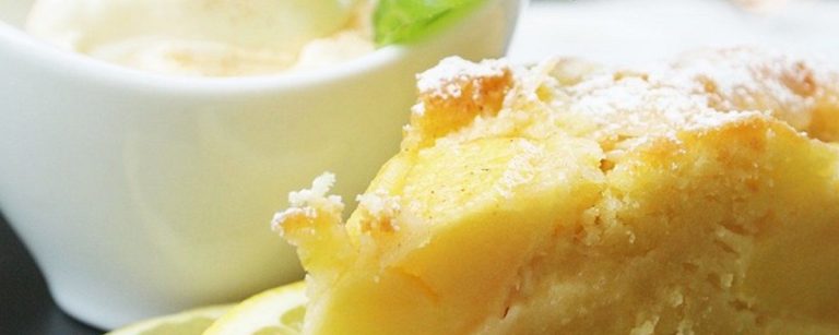 Ein Stück Zitronenkuchen bestäubt mit Puderzucker, serviert mit Eis und einer Zitronenscheibe.