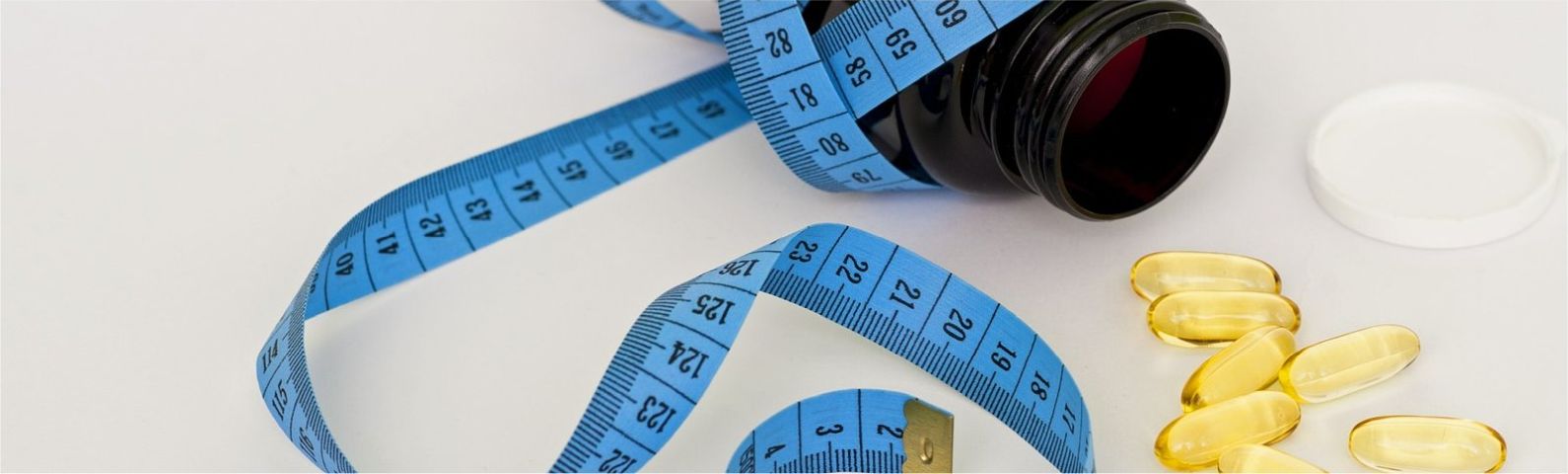 Blaues Maßband mit Pillen und Pillendose, symbolisiert Gewichtsverlust und gesunde Ernährung.