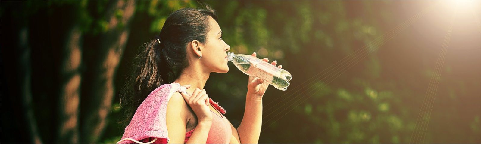 Junge Frau trinkt nach dem Sport Wasser in der Natur.