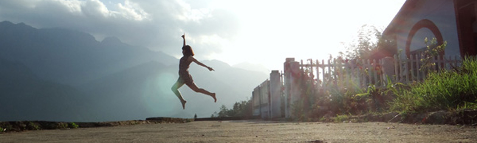 wanneer-raak-je-uit-shape Junge Frau springt voller Energie im Freien mit Bergen im Hintergrund – Symbol für einen aktiven Lebensstil.
