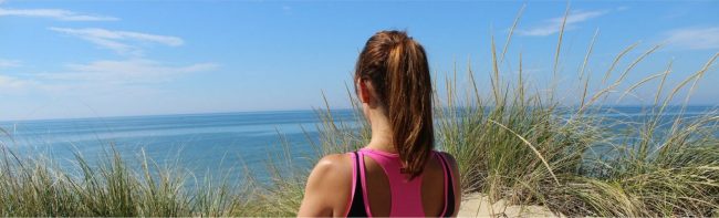 Frau mit Pferdeschwanz blickt aufs Meer, trainiert für gesunde Ernährung.