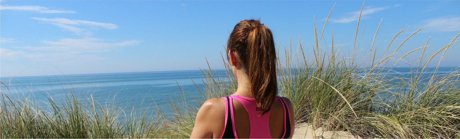 yoga-groot Frau mit Pferdeschwanz blickt aufs Meer, trainiert für gesunde Ernährung.