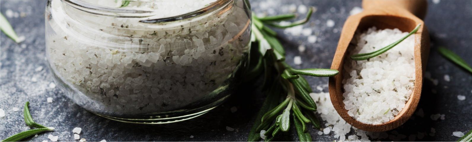 Grobes Salz mit Rosmarin in einem Glas und Holzlöffel für gesunde Ernährung.