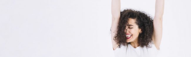 Frau mit Locken und roten Lippen, die lacht, vor weißem Hintergrund für Fitness-Ernährung.