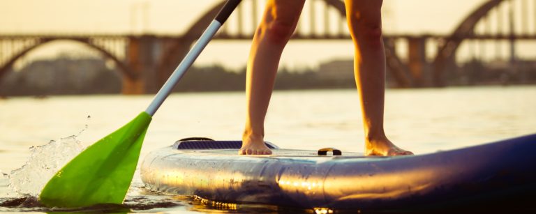 Eine Frau steht auf einem SUP-Board im Wasser und paddelt.