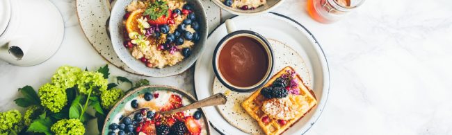 Gesunde Frühstücksschüssel mit Obst, Haferflocken, Beeren, Waffeln und Kaffee.