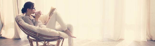 Frau im Sessel liest und trinkt, entspannt und ernährt sich gesund.