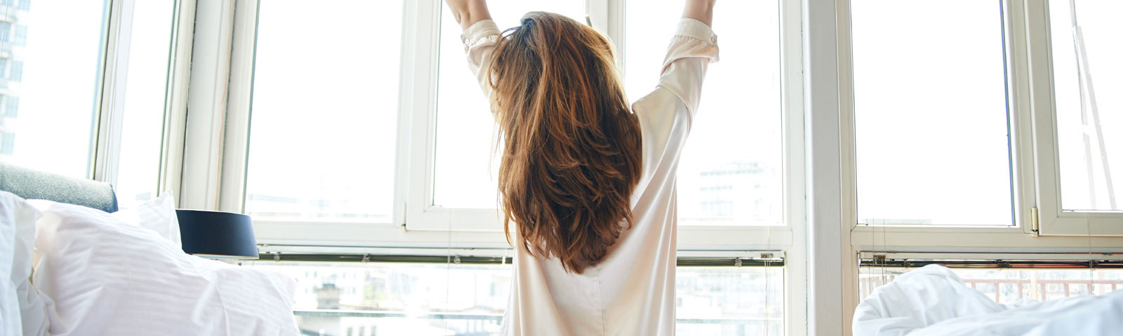 2022_05_beweeg Frau streckt sich im Bett vor einem hellen Fenster, bereit für einen energiegeladenen Tag – perfekt für Fitness- und Ernährungsprogramme.