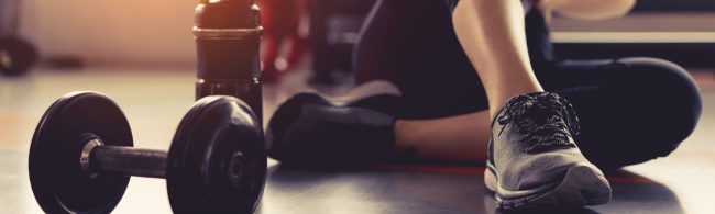 Dumbbells, Wasserflasche und Beine im Fitnessstudio, bereit für ein Training, ideal für Fitness-Ernährungsunternehmen.