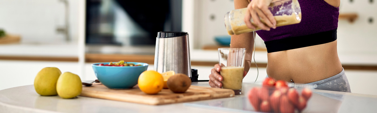 Hoe-snel-wen-je-aan-gezondere_leefstijl Frau macht Smoothie in der Küche, gesunde Ernährung für Fitness.