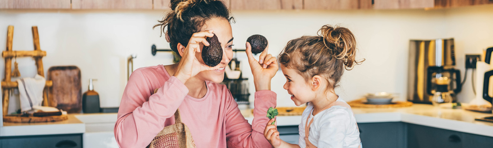 Mutter und Kind spielen mit Avocados in der Küche und lernen gesunde Ernährung.