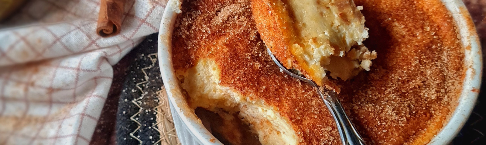 Slice of pear churro cheesecake with glossy caramelised pear wedges on top and a cinnamon-sugar crumb edge on a white plate.