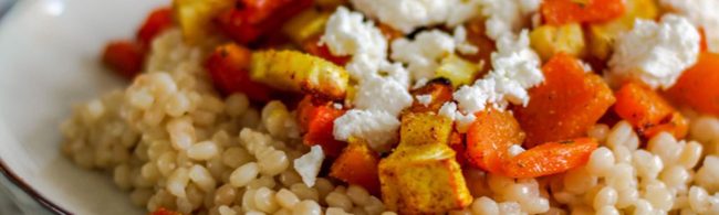 Pearl couscous salad with roasted vegetables, cherry tomatoes and fresh herbs in a bowl, drizzled with lemon-olive oil dressing.