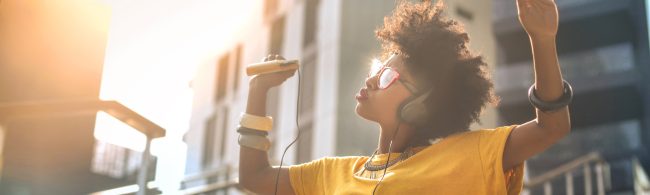 Person relaxing with headphones in a cozy room at dusk, soft warm lighting and a calm playlist on a phone screen.