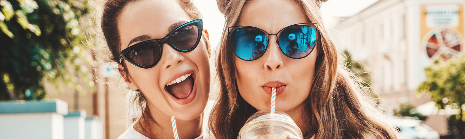 stressvrij-afvallen Zwei junge Frauen in Sonnenbrillen trinken gesunde Smoothies im Freien.