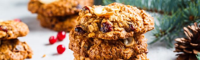 A stack of golden-brown oatmeal Christmas cookies with cranberries and chopped nuts, placed on a festive baking sheet.