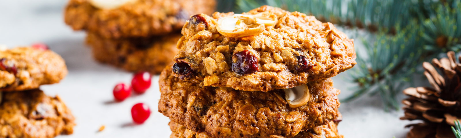 A stack of golden-brown oatmeal Christmas cookies with cranberries and chopped nuts, placed on a festive baking sheet.