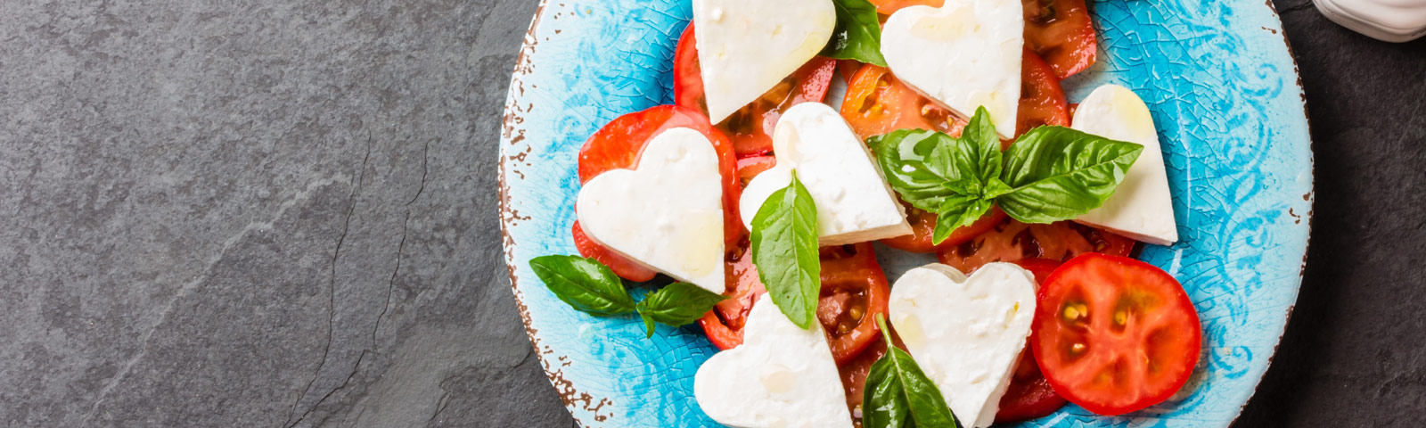A plated three-course meal for Valentine’s Day featuring heart-shaped mozzarella Caprese salad, herbed grilled chicken with lemon, and chocolate-covered fruit treats.